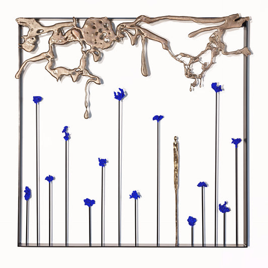 A metal wall sculpture with an abstract gold top section and vertical rods with blue flowers arranged inside a square black frame.