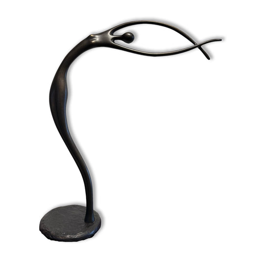 A sleek, abstract black sculpture resembling a slender, elongated figure with outstretched arms balanced on a round base.