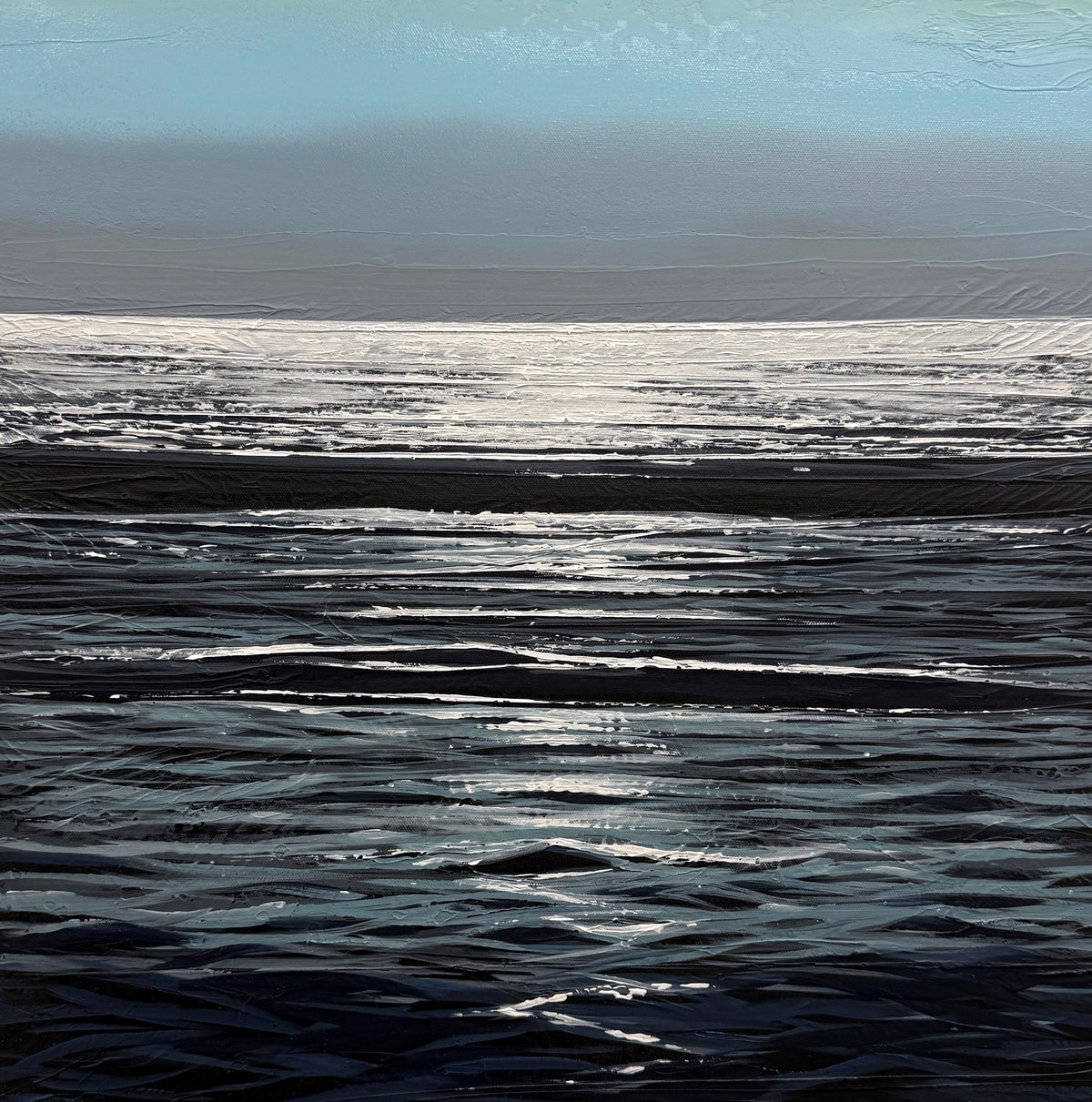 Sunlight reflects off gentle waves on a calm ocean under a blue sky, with the horizon visible in the distance.