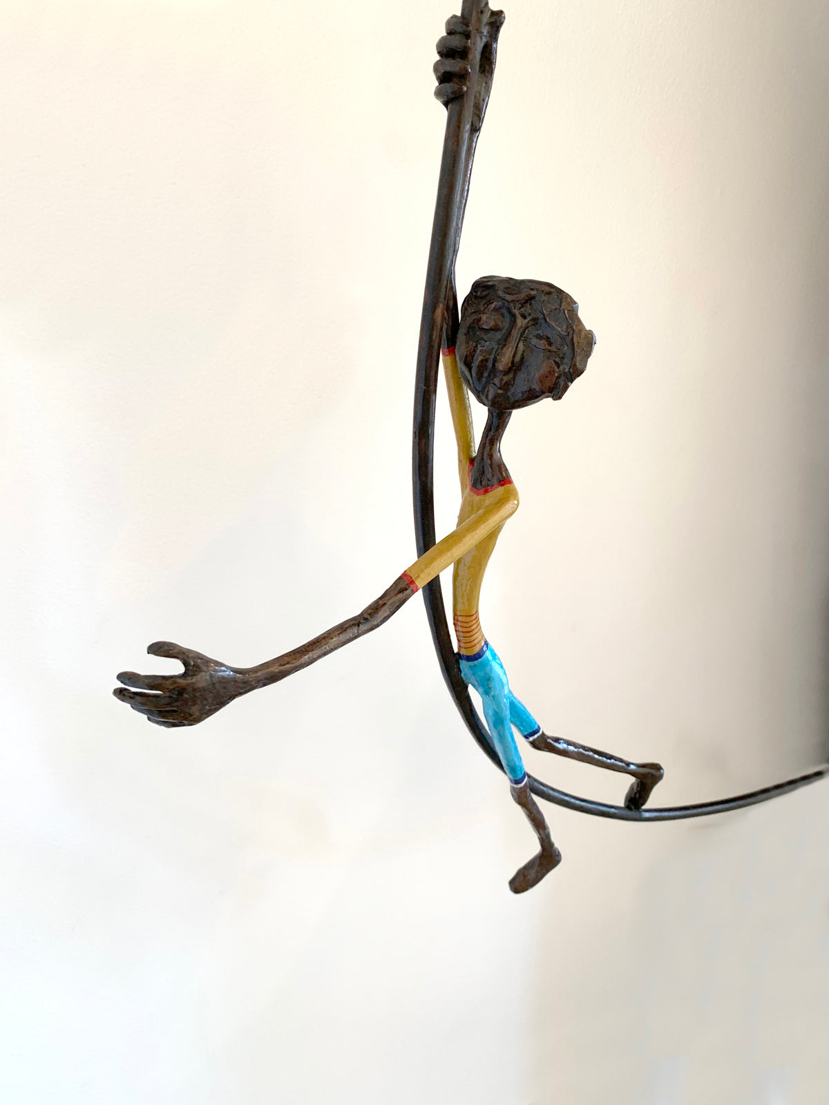 A minimalist sculpture of a figure holding onto a large red balloon. The figure appears to be airborne, with legs dangling and arms extended upward gripping the string. (view 2)