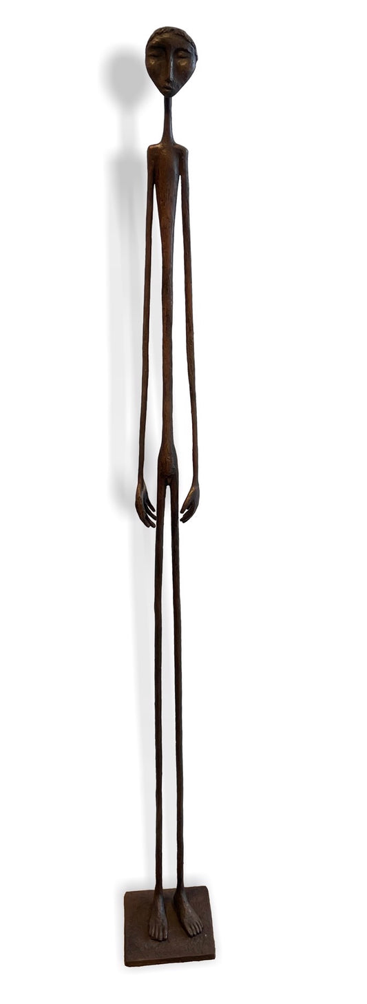 Tall, slender bronze sculpture of a human figure with elongated limbs, standing on a rectangular base. The figure has minimal facial features and an abstract, stylized form.