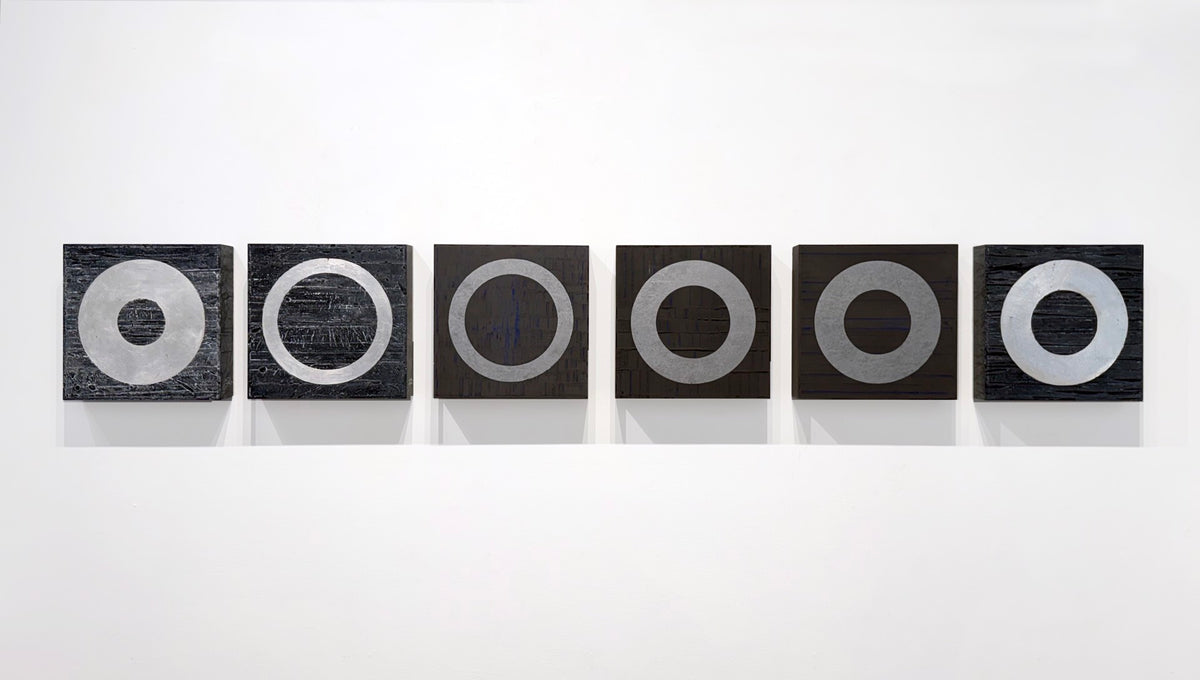 Six black squares with silver rings lined up on a white wall.