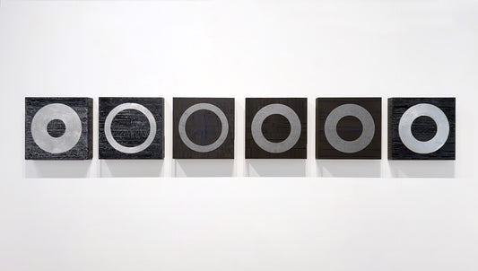 Six black squares with silver rings lined up on a white wall.