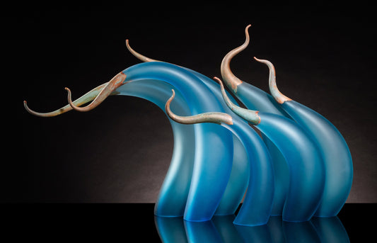Curved blue glass sculptures with bronze, horn-like tips on a black background.