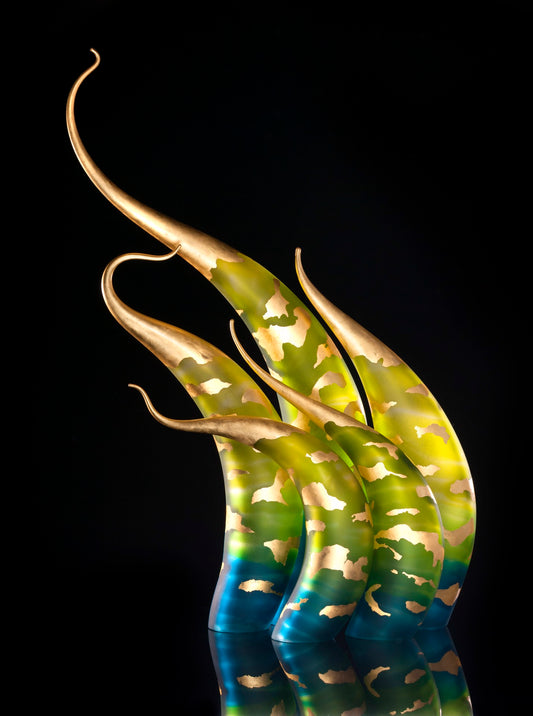 Five abstract glass sculptures with gold, green, and blue tones, featuring curved, elongated shapes and metallic patches, set against a black background.