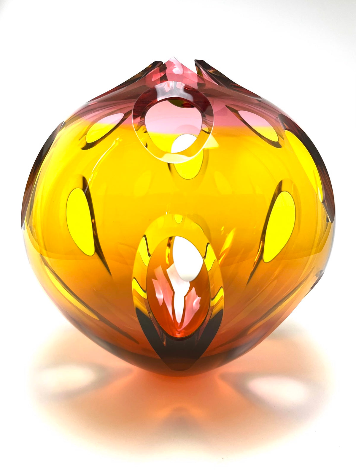 Glass sculpture in yellow and pink tones with oval cutouts and a glossy surface.