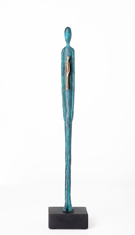 Tall, slender teal sculpture of a standing human figure with a smaller silver figure embedded in its chest, displayed on a black rectangular base.