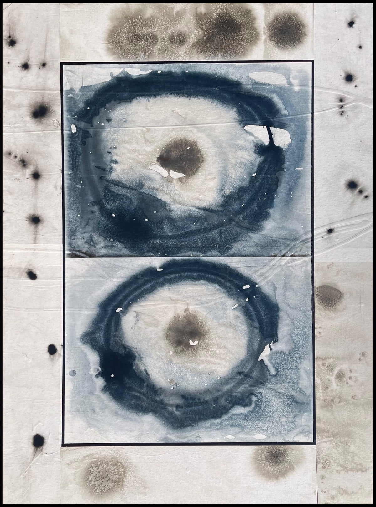 Abstract artwork featuring two large, circular ink patterns with dark centers, surrounded by scattered black spots on a white background.