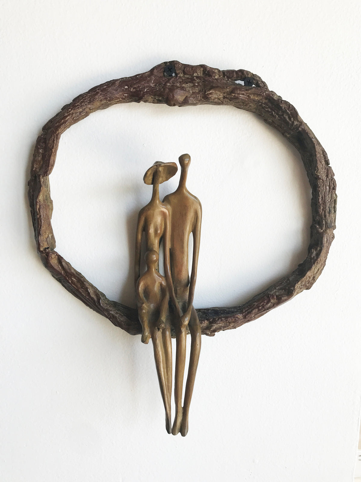 Bronze sculpture of three abstract human figures sitting together inside an oval frame resembling a tree branch.