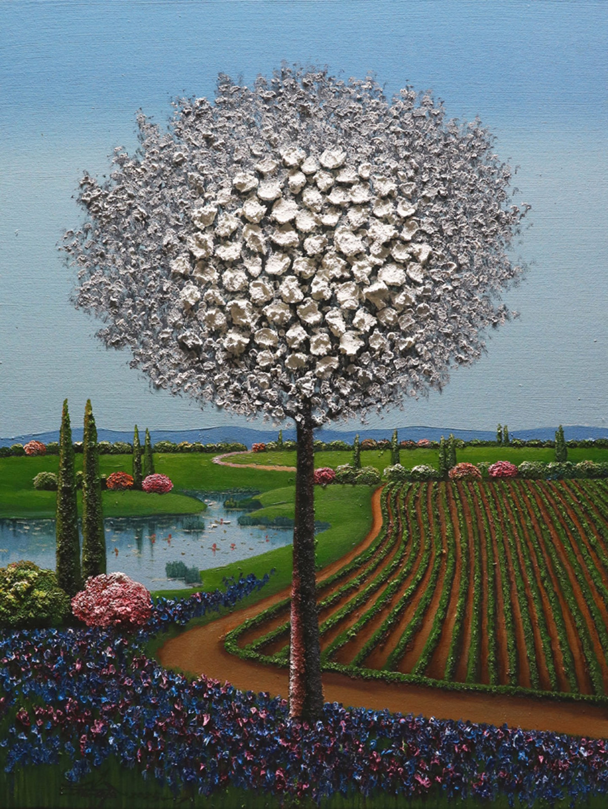 A tree with a large, spherical, white blossom stands by a lake amid fields and gardens under a clear blue sky.