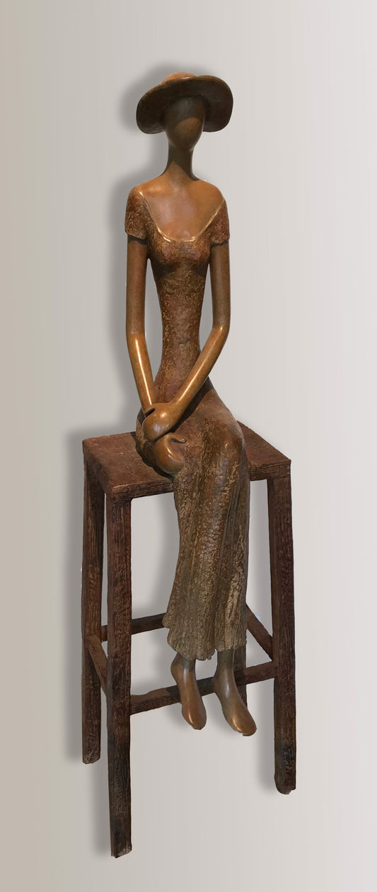 A bronze sculpture of a faceless woman wearing a long dress and wide-brimmed hat, sitting with her hands clasped on a wooden high stool.