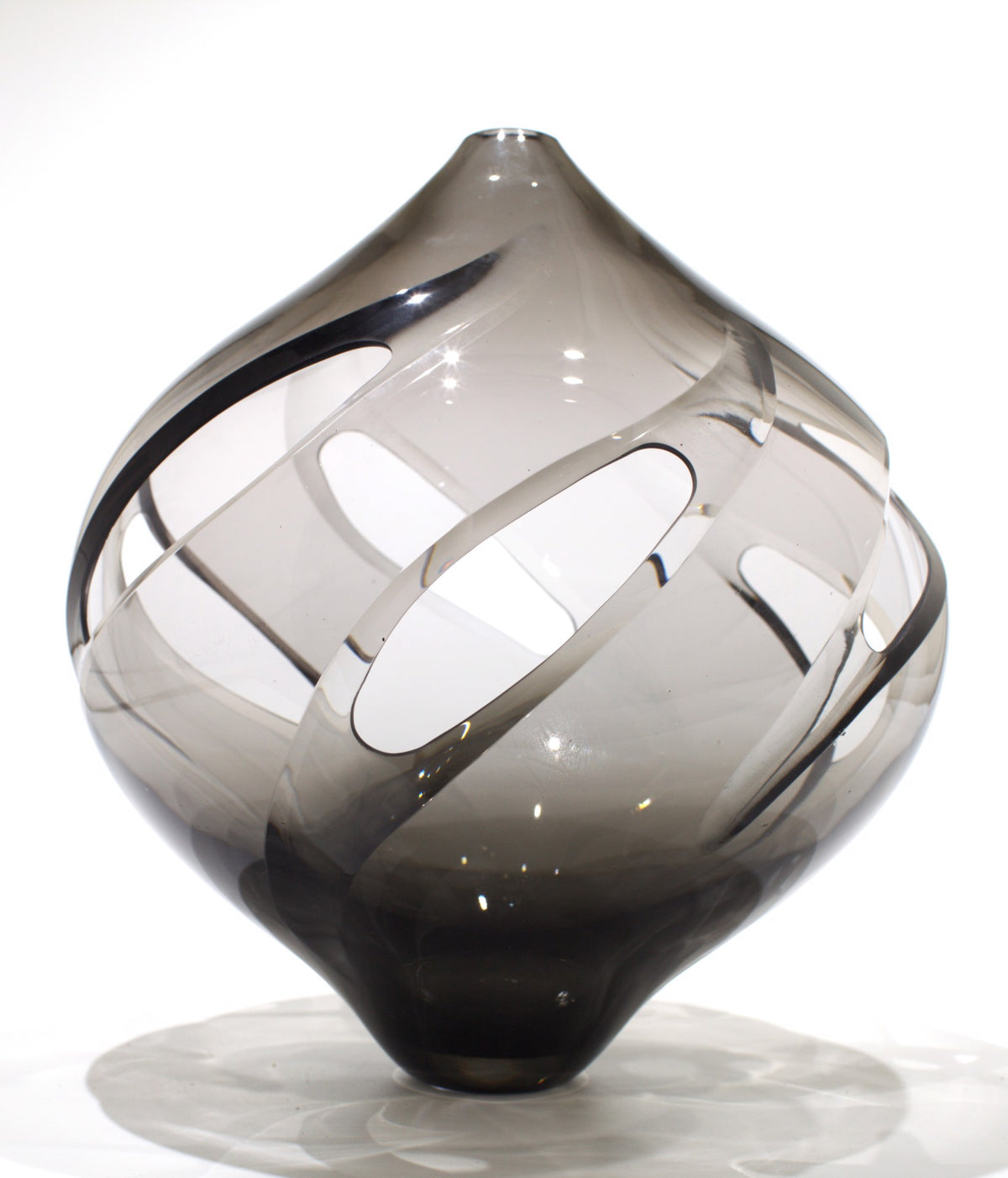 Smoky gray glass sculpture with a spiral of oval cutouts on a white background.