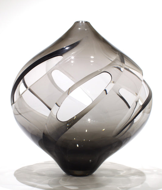 Smoky gray glass sculpture with a spiral of oval cutouts on a white background.