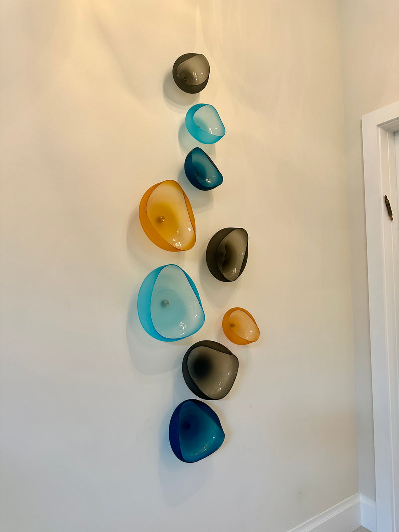The Goodman Studio blown glass wall sculpture of amber, aqua, cobalt and smoke-gray bowls in a white entry hall