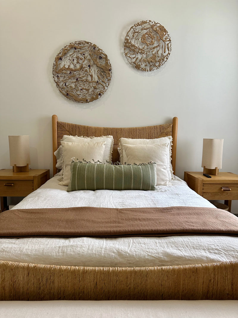 Pair of round Jennyfer Stratman wall sculptures above a woven headboard in a natural coastal bedroom