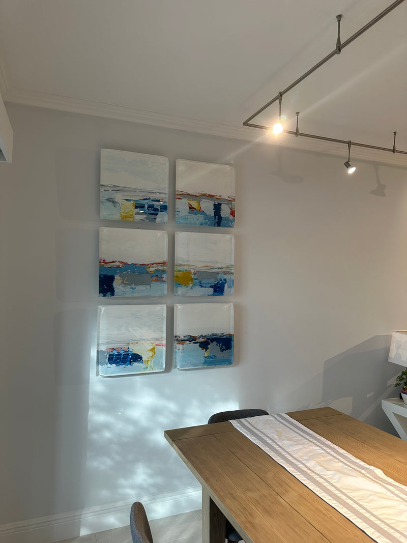 Six small John Schuyler abstract seascapes in blue, white and yellow hung as a grid in a dining area