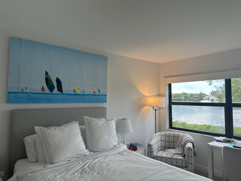Peter Kuttner painting of colorful sailboats on a blue sea above a bed in a lakeside South Florida bedroom
