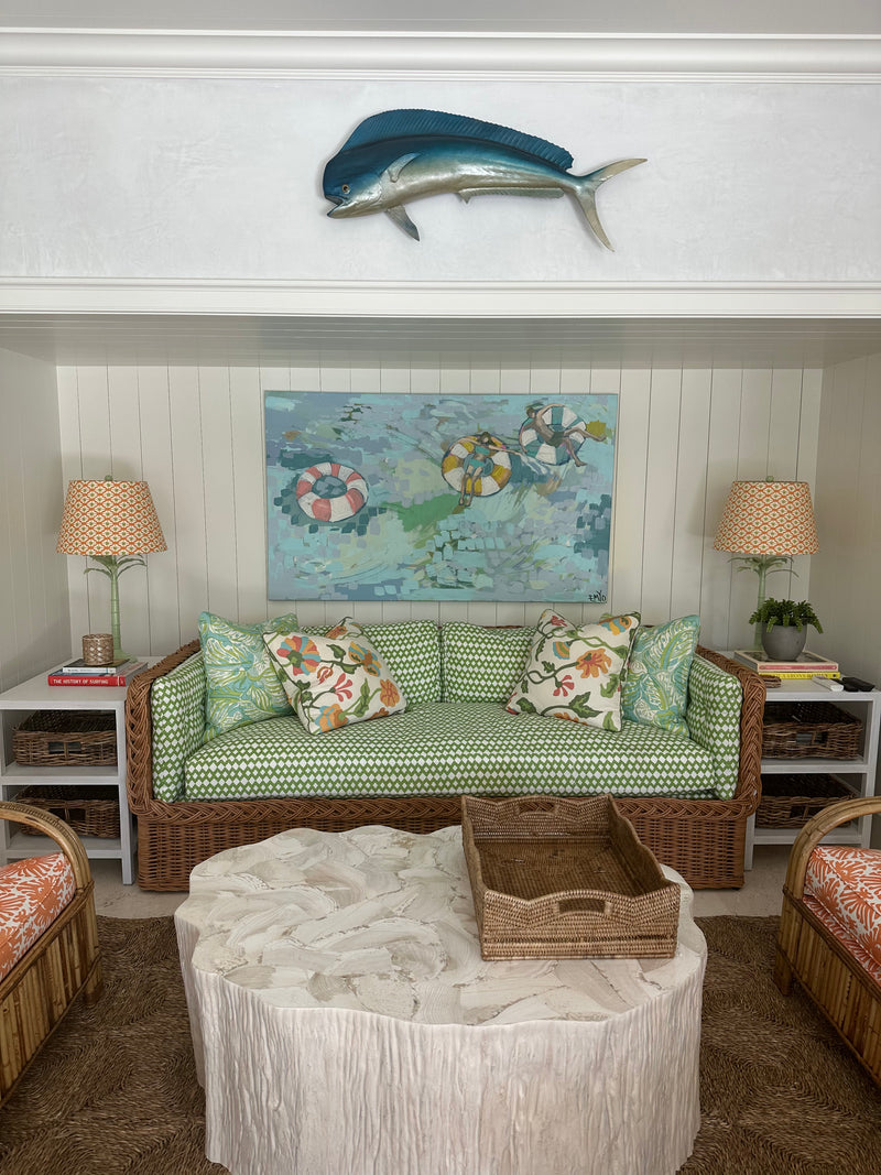 Emyo painting of pool floats in turquoise water above a green wicker sofa in a coastal Florida lounge