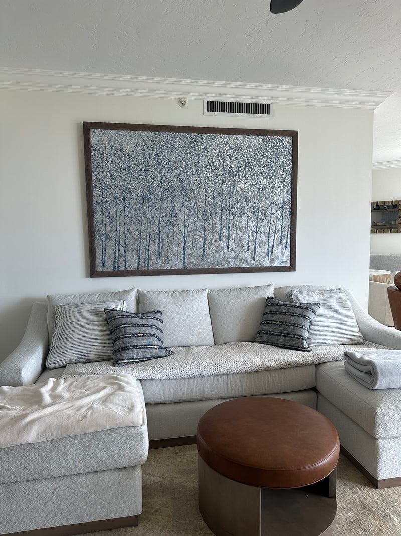 Barrett Edwards silver and blue birch forest painting above a white sectional sofa in a condo living room