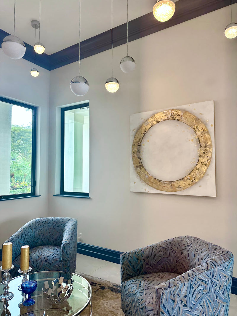 Takefumi Hori gold leaf circle artwork in a sitting room with blue swivel chairs and globe pendant lights