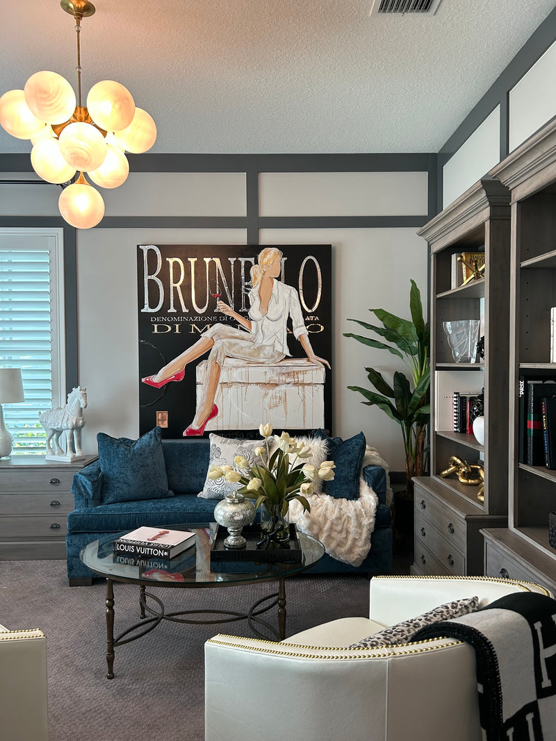 Large fashion painting by Vincent Cordo of a woman in a white suit seated on a Brunello sign, in a navy and gray living room