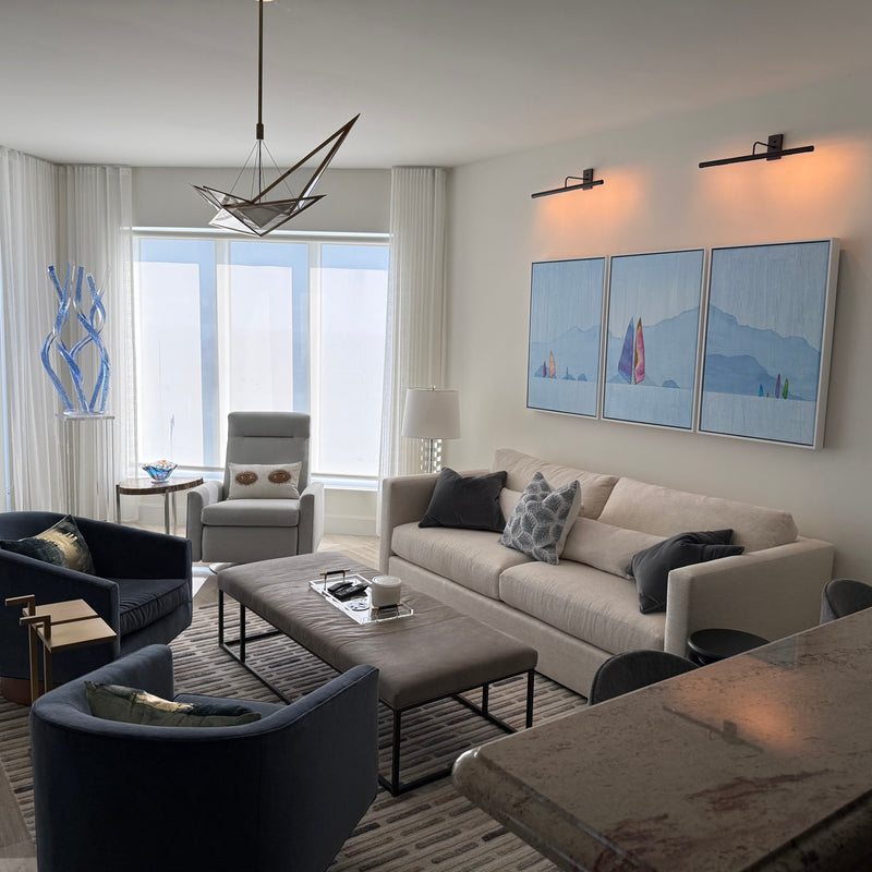 Three-panel painting by Peter Kuttner of colorful sailboats against blue mountains above a sofa in a modern living room