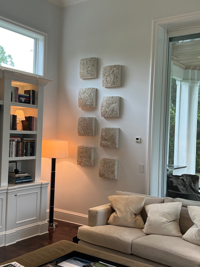 Gregor Turk sculptural relief tiles hung in a vertical pattern beside built-in bookshelves in a living room