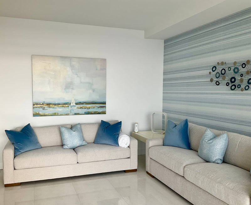 Alma Ramirez coastal landscape with a sailboat in soft blues and gold above a sofa in a light blue living room