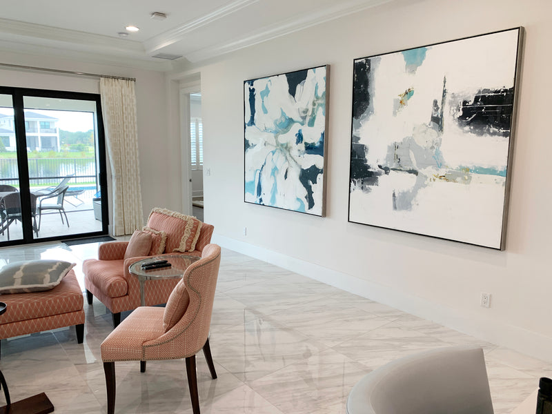 Two large John Schuyler abstract paintings in white, teal and black in a bright living room with lake views
