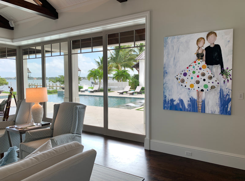 Kim Schuessler painting of a couple, she in a polka-dot dress, in a living room overlooking a pool and the water