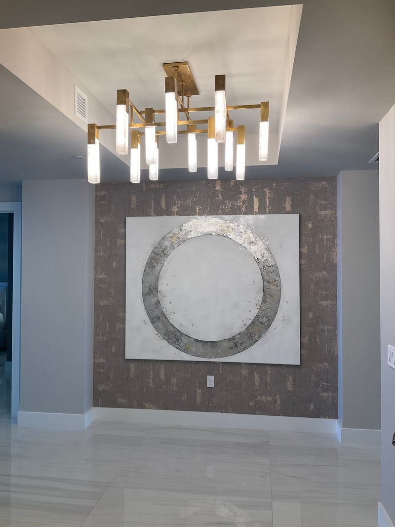 Takefumi Hori silver leaf circle artwork on a textured accent wall under a brass chandelier, condo foyer