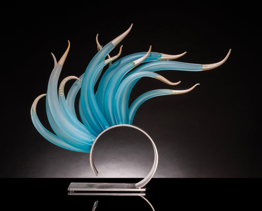 Curved blue glass sculpture with gold tips on a circular base, black background.