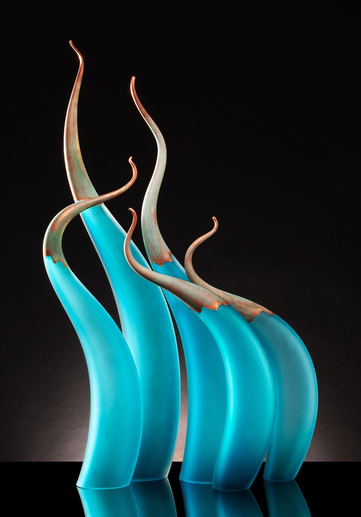Four tall, curved blue and copper glass sculptures on a black background.