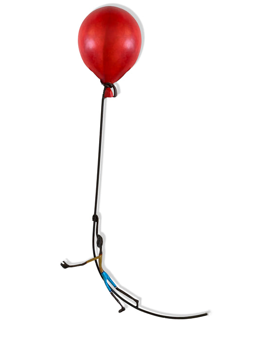 A minimalist sculpture of a figure holding onto a large red balloon. The figure appears to be airborne, with legs dangling and arms extended upward gripping the string.