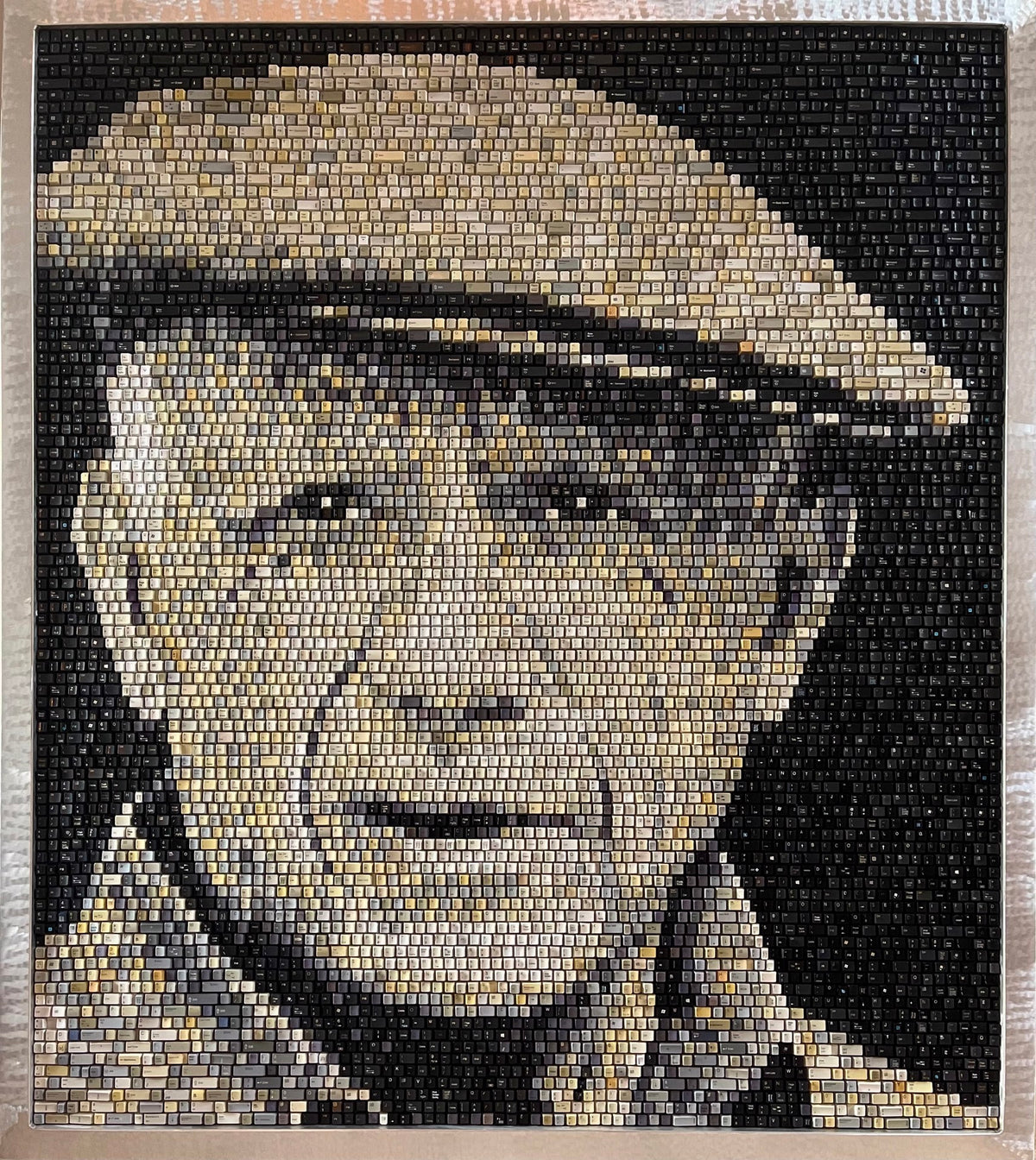A mosaic portrait of artist Pablo Picasso wearing a flat cap, created entirely out of upcycled computer keyboard keys by Doug Powell.