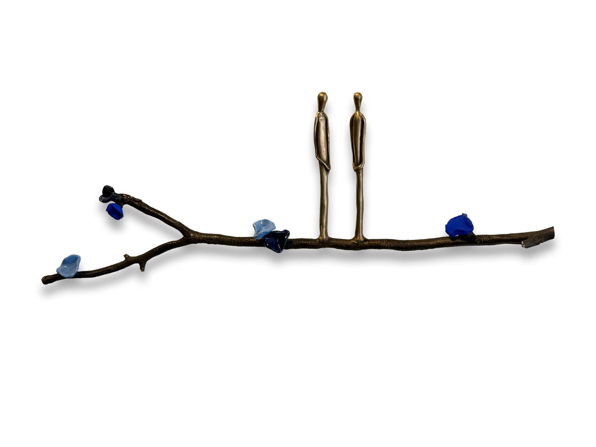 Two metal figures stand on a branch with blue stones against a white background.