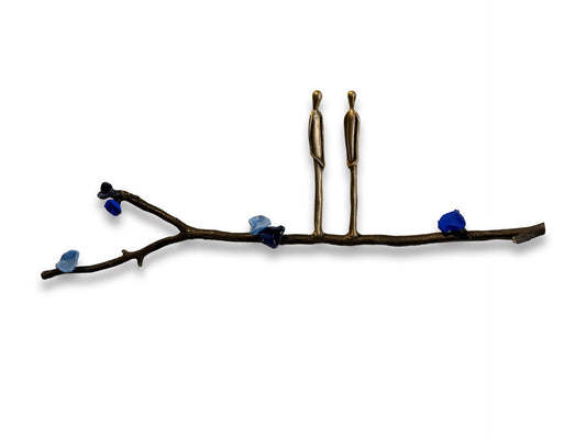 Two metal figures stand on a branch with blue stones against a white background.