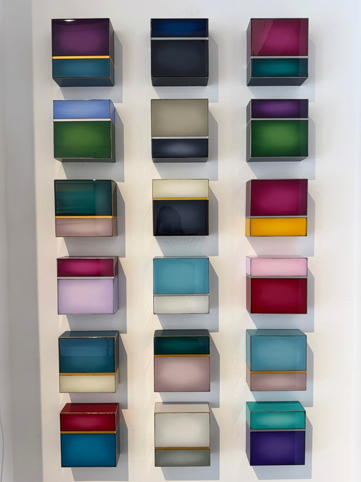 Sixteen colorful, translucent wall-mounted boxes arranged in a grid pattern.