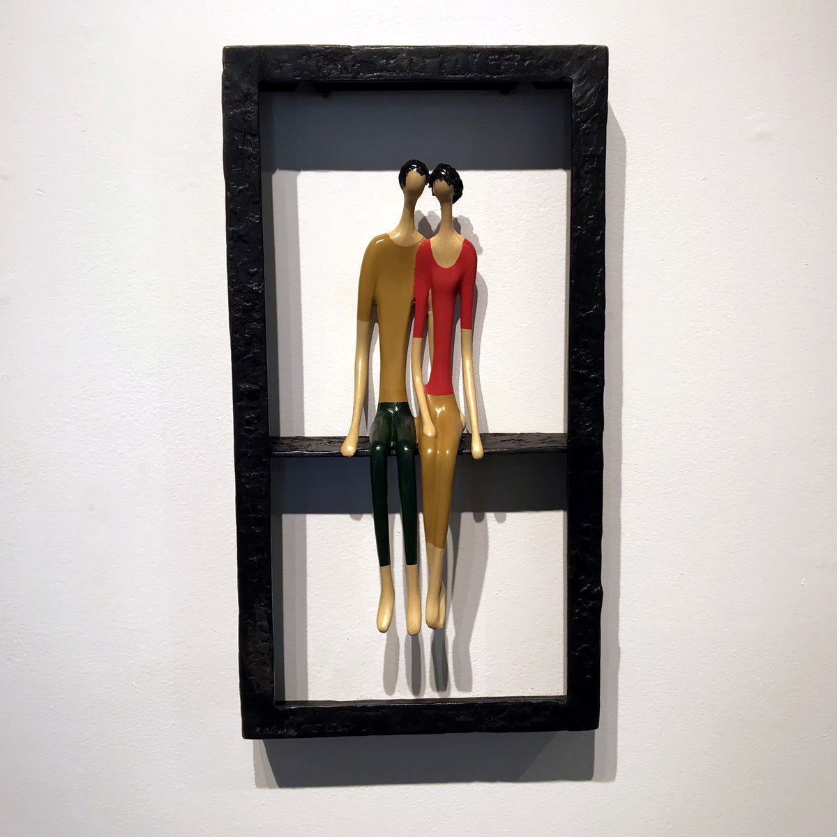 Two abstract, elongated figures in vibrant colors sit within a rectangular black frame, mounted on a white wall.
