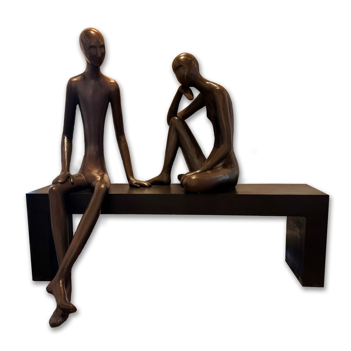 Two abstract, bronze-colored human figures sit on a simple black bench. One figure sits upright, while the other has a hand resting on its knee, appearing contemplative.