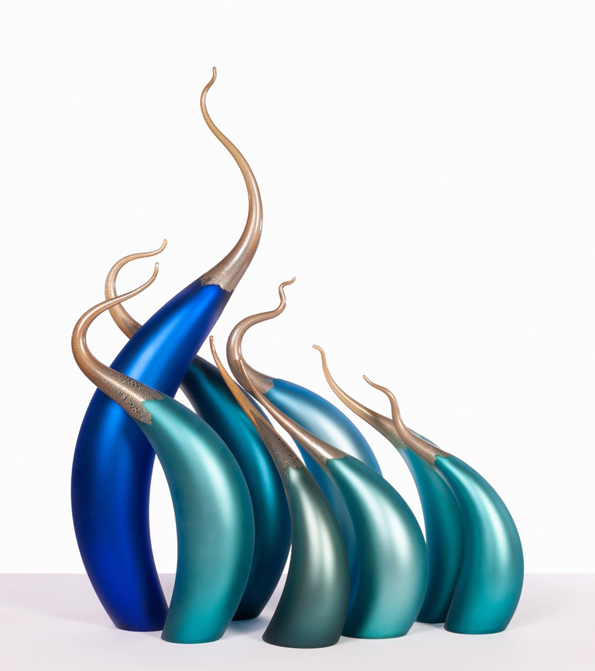 Curved blue and teal glass sculptures with gold wispy tips on a white background.